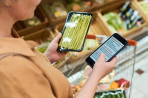 Frau prüft im Supermarkt ein Produkt mit dem Smartphone