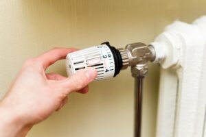 Hand dreht an einem Heizkörperthermostat, die Zahlenskala von 1 bis 5 ist zu sehen
