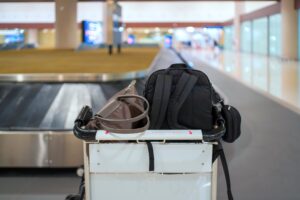 Gepäckwagen mit Reisetaschen und Rucksack am Gepäckband eines Flughafens