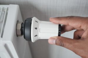 Eine Hand stellt das Thermostat an einem weissen Heizkoerper ein