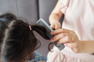 Erwachsene Hand kämmt einem Kind mit dunklen Haaren die Strähnen mit einem feinen Kamm durch