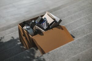 Ein offener Umzugskarton mit ausrangierten Gegenständen steht draußen auf einer Treppenstufe.