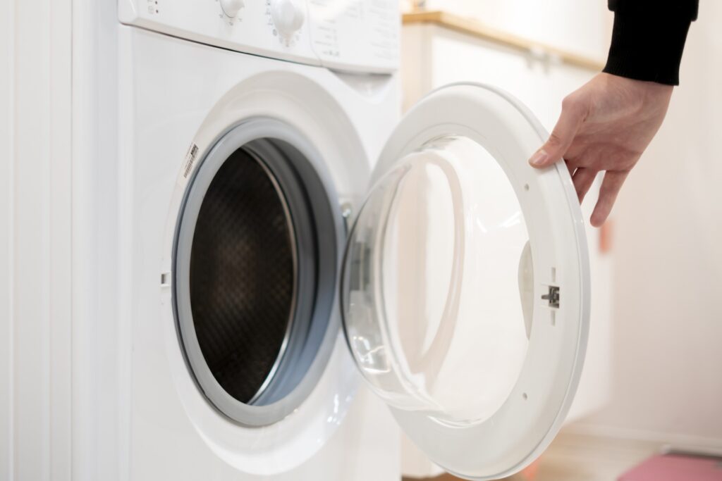 Hand öffnet die Tür einer weißen Waschmaschine im Badezimmer