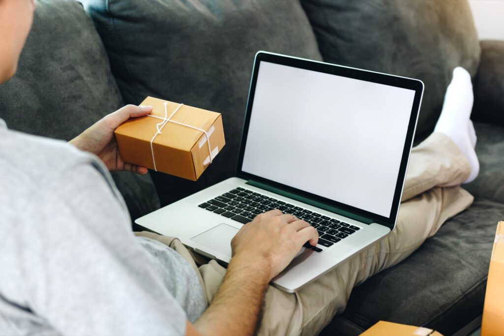 Mann sitzt mit Laptop auf dem Sofa und hält ein Paket in der Hand