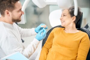 Zahnarzt zeigt einer lächelnden Patientin im Behandlungsstuhl ein Zahnmodell