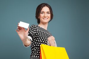 Lächelnde Frau hält eine weiße Kundenkarte in die Kamera, in der anderen Hand trägt sie eine gelbe Einkaufstüte