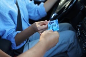 Eine Hand reicht im Auto einer Person am Steuer einen Führerschein im Kartenformat