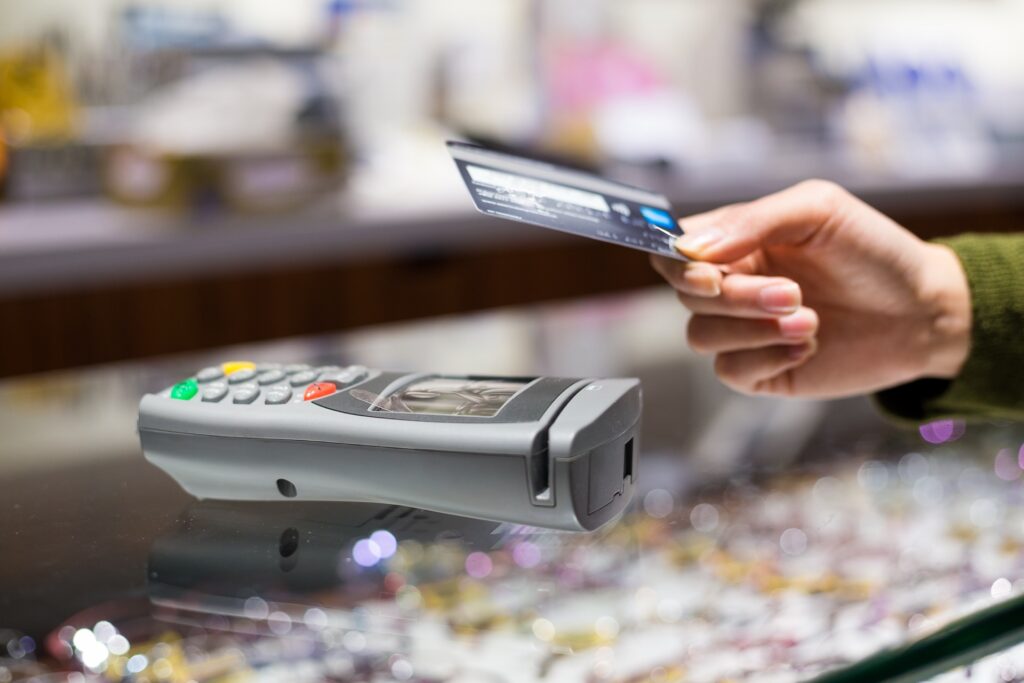 Hand hält eine Kreditkarte kontaktlos an ein Kartenterminal auf einer Ladentheke