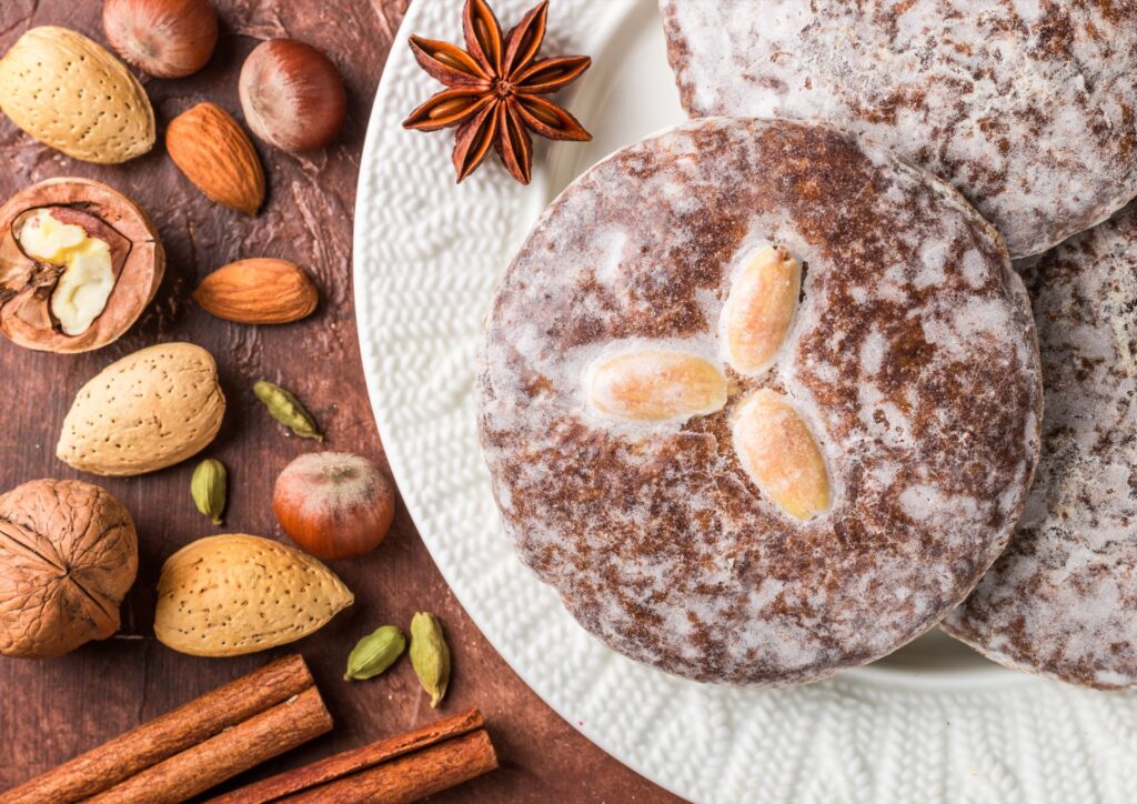 Glasierte Nürnberger Lebkuchen mit Mandeln auf einem Teller, daneben Haselnüsse, Walnüsse, Mandeln, Sternanis und Zimtstangen
