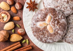 Glasierte Nürnberger Lebkuchen mit Mandeln auf einem Teller, daneben Haselnüsse, Walnüsse, Mandeln, Sternanis und Zimtstangen