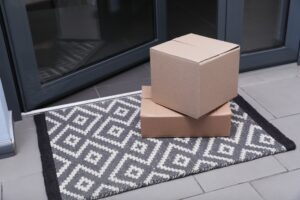 Zwei Pappkartons liegen auf einer gemusterten Fußmatte vor einer Haustür