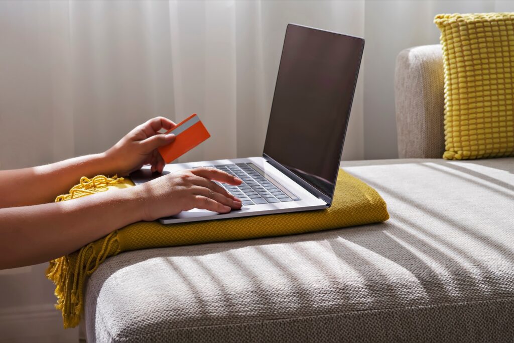 Eine Frau sitzt mit einem Laptop auf dem Sofa und hält eine Kreditkarte in der Hand, während sie online einkauft