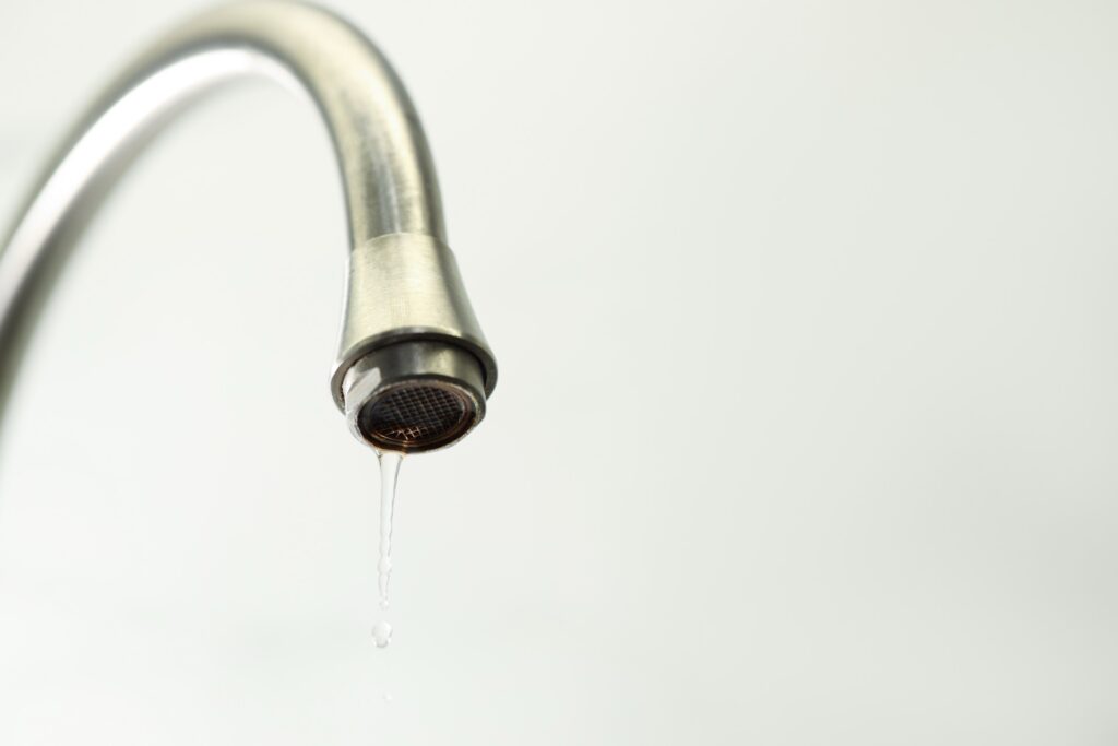Ein silberner Wasserhahn, aus dem nur noch ein dünner Wasserstrahl tropft
